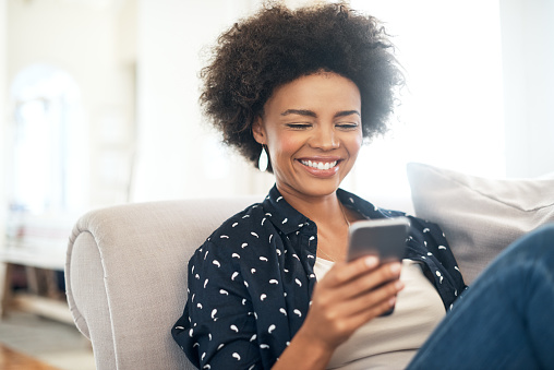 Black woman smiling and looking at cell phone on couch 