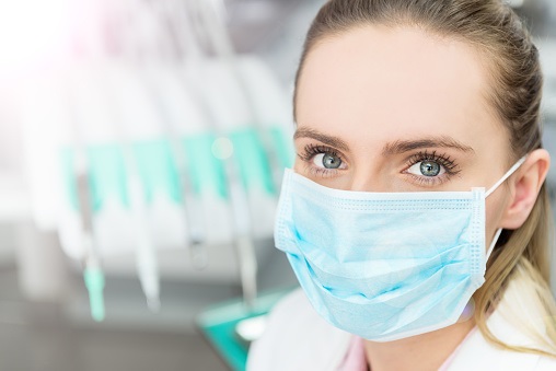 Horizontal close-up color image of female medicine doctor looking at camera and wearing blue surgical mask.